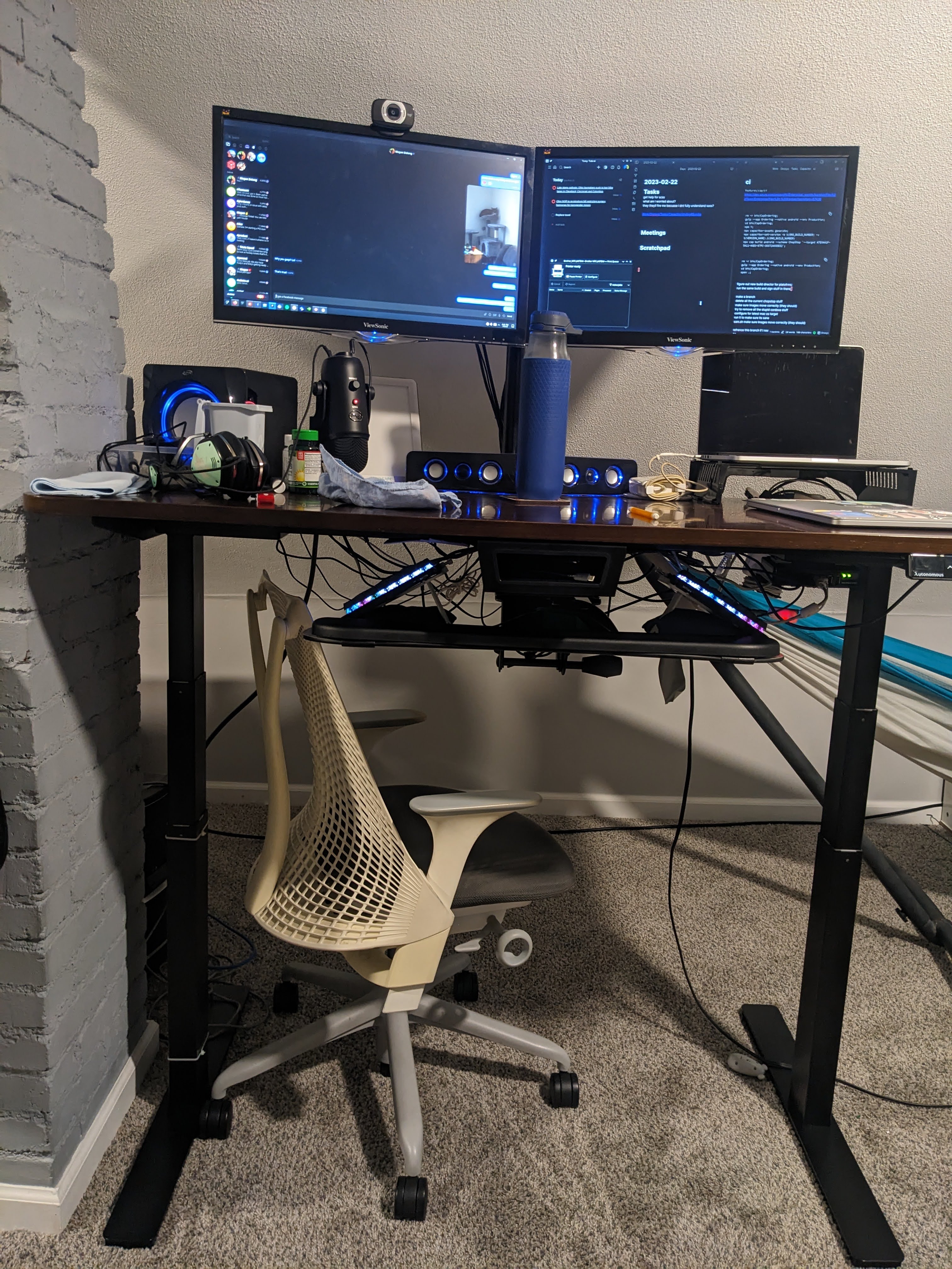 a standing desk next to a chimney.  it has a strange keyboard and two monitors
